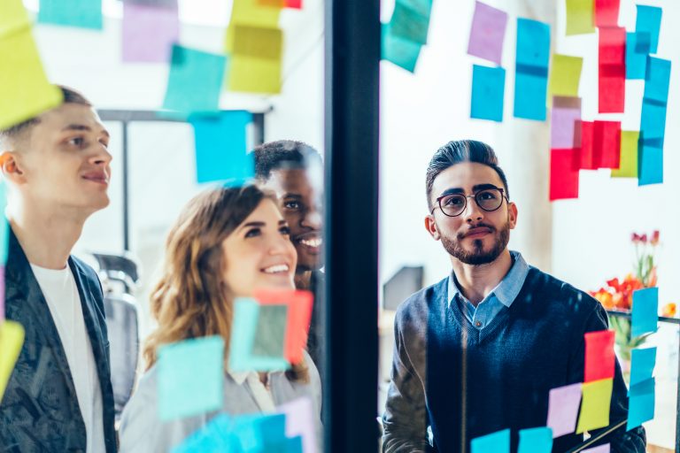 Joyful employee reading notes on glass wall with coworkers